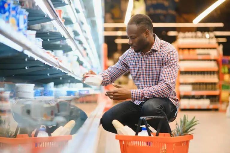 A man is lifting a plastic container from a refrigerator in a grocery store